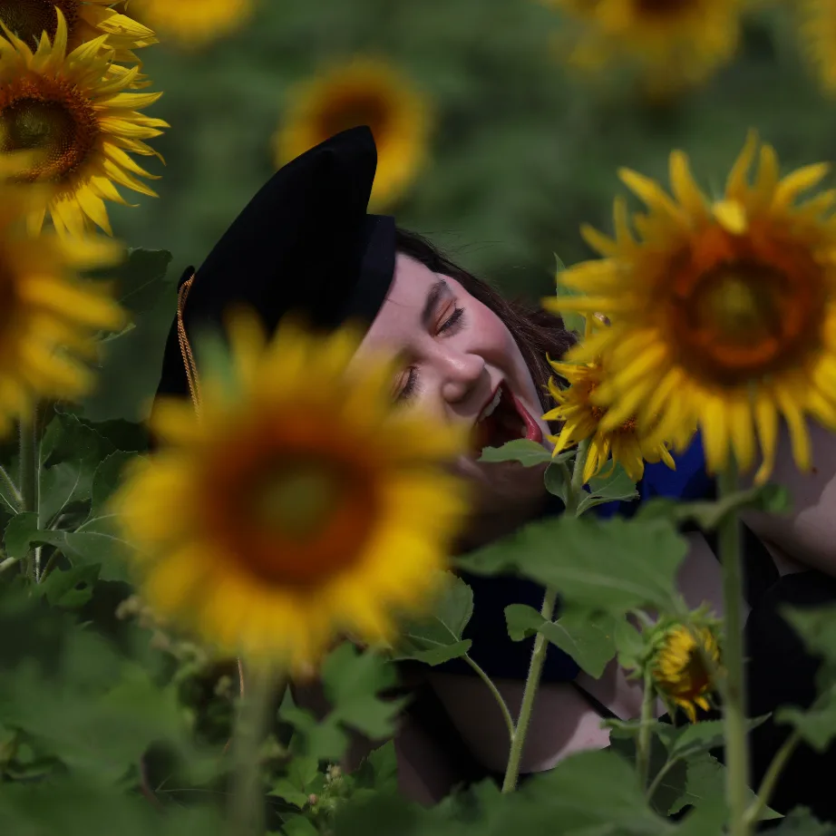 Sadie Nickles in a graduation cap, laughing in a field of sunflowers